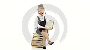 Smart little girl is studying an encyclopedia sitting on books