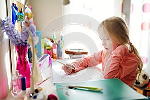 Smart little schoolgirl doing her homework at her table at home. Child learning to write and read