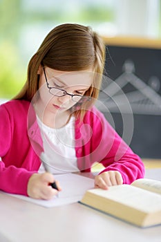 Smart little schoolgirl with pen and books writing a test in a classroom