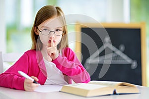 Smart little schoolgirl with pen and books writing a test in a classroom