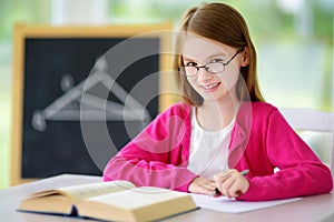 Smart little schoolgirl with pen and books writing a test in a classroom