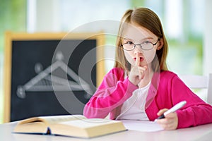 Smart little schoolgirl with pen and books writing a test in a classroom