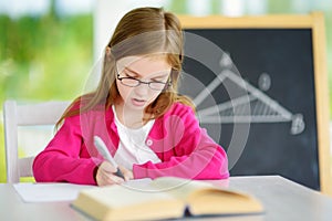 Smart little schoolgirl with pen and books writing a test in a classroom. Child in an elementary school.