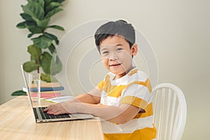 Smart looking Asian preteen boy writing and using computer laptop studying online lessons