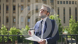 Smart male financial analytic in round glasses and suit, with cup of coffee, considering current market trends