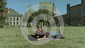 Smart male student working on laptop on campus lawn