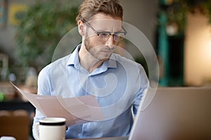 Smart man with drafts in his hand working at laptop.