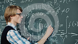 Smart man writing equations on blackboard in class focused on mathematics