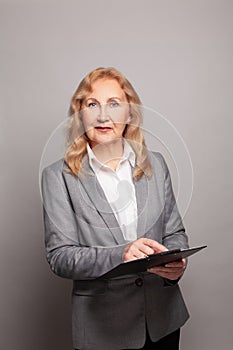 Smart mature senior business woman smiling and holding folder on grey background