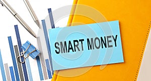 SMART MONEY text on sticker on the yellow notebook with chart and pen