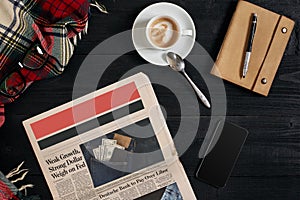 Smart phone with black display on wooden background. Newspaper and coffee on wooden table. Top view.