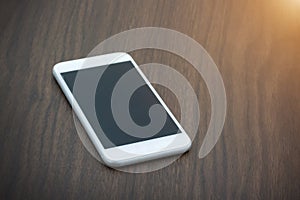 Smart phone with blank screen lying on wooden table