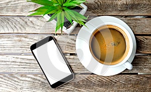 Smart phone and coffee cup with flowerpot on wooden table.