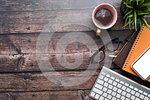 Smart phone, coffee cup, notebook, glasses, keyboard on wooden desk.