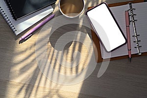 Smart phone, coffee cup and notebook on wooden table near window.