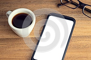 Smart phone on desk with white screen, eyeglasses and cup of coffee on wooden table