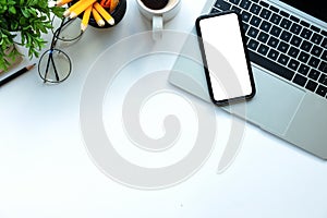 Smart phone, laptop computer, coffee cup and glasses on white table. Flat lay