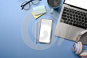 Smart phone, laptop, headphone, sticky notes and coffee cup on blue background.