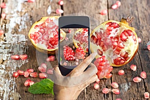 Smart phone take photos of pomegranate on wooden background