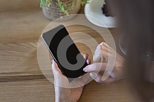 Smart phone in woman hands against on wooden table background. Smartphone with blank black screen. Copy space