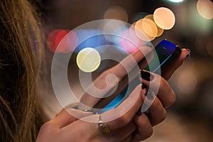 Smart phone in woman hands in front of blurred city lights