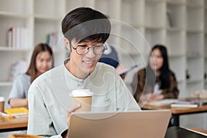 A smart, positive Asian male university student focusing on his work on laptop computer