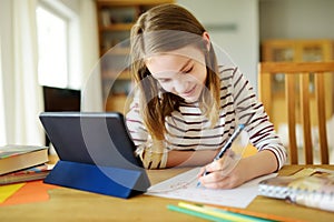 Smart preteen schoolgirl doing her homework with digital tablet at home. Education and distance learning for kids. Homeschooling photo