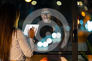 Smart pretty business woman taking a break while cheaking her digital tablet standing in the office at night