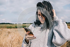 Smart and pretty Caucasian woman texting on mobile phone, using wireless connection for social life, posing outside with windy