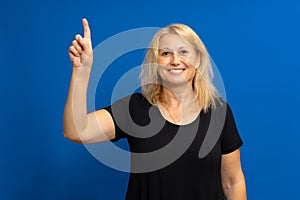 Smart proactive 40 years old woman in black t-shirt holding up index finger with great new idea isolated on blue colored photo