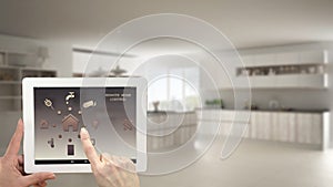 Smart remote home control system on a digital tablet. Device with app icons. Blurry interior of minimalist kitchen in the backgrou