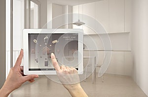 Smart remote home control system on a digital tablet. Device with app icons. Interior of minimalist white kitchen in the backgroun