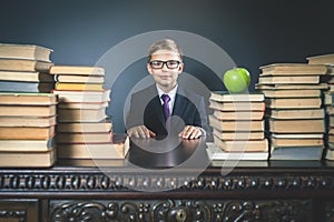 Smart school boy sitting at table with many books