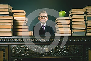 Smart school boy sitting at table with many books