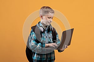 Smart schoolboy with backpack and headset holding laptop