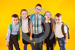 Smart schoolchildren smiling and looking at camera over yellow background. Happy kids in school uniform with backpacks