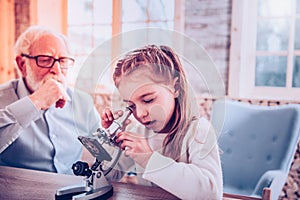 Smart schooler with nice hairstyle using microscope