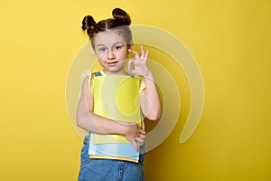 Smart schoolkid girl shows OK hand sign, smiling at camera, feeling happy to start a new semester in new primary school