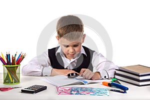 Smart serious pupil at the desk exploring with magnifier on the clean white background