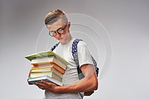 Smart student in glasses with a backpack and a stack of books in his hands