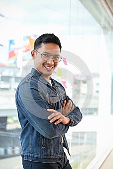 Smart and talented Asian businessman arms crossed, leaning on the glass wall