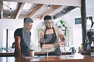 The smart tech that keeps their sales up. two young men using a digital tablet while working in a cafe.