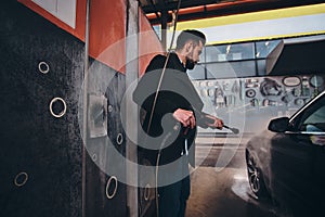 Smart trendy man in jeans and blaser is washing his own car at car washing station