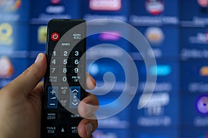 Smart tv and hand pressing remote control.Hand holding TV remote control with a television in the background. Close up