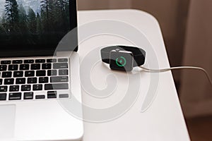 Smart watch on wireless charging with on-screen charging indicator. Work place near at the laptop