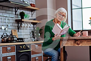 Smart white-haired lady in years making notes of vedic books