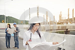 Smart woman engineer holding white hard hat on hand and look at refinery industry plant at industry factory center area.