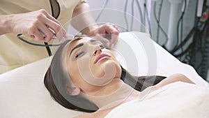 Smart woman getting ultrasonic face procedure in beauty parlor