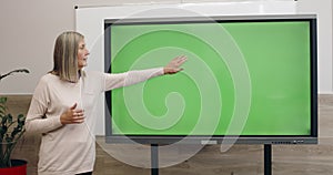 Smart woman talking while using and touching interactive screen with template green screen. Female professor explaining