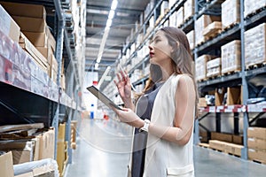 Smart young Asian businesswoman checking goods on shelves with digital tablet